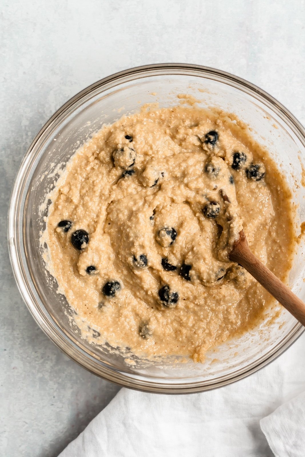 healthy blueberry oatmeal muffin batter being mixed in a glass bowl
